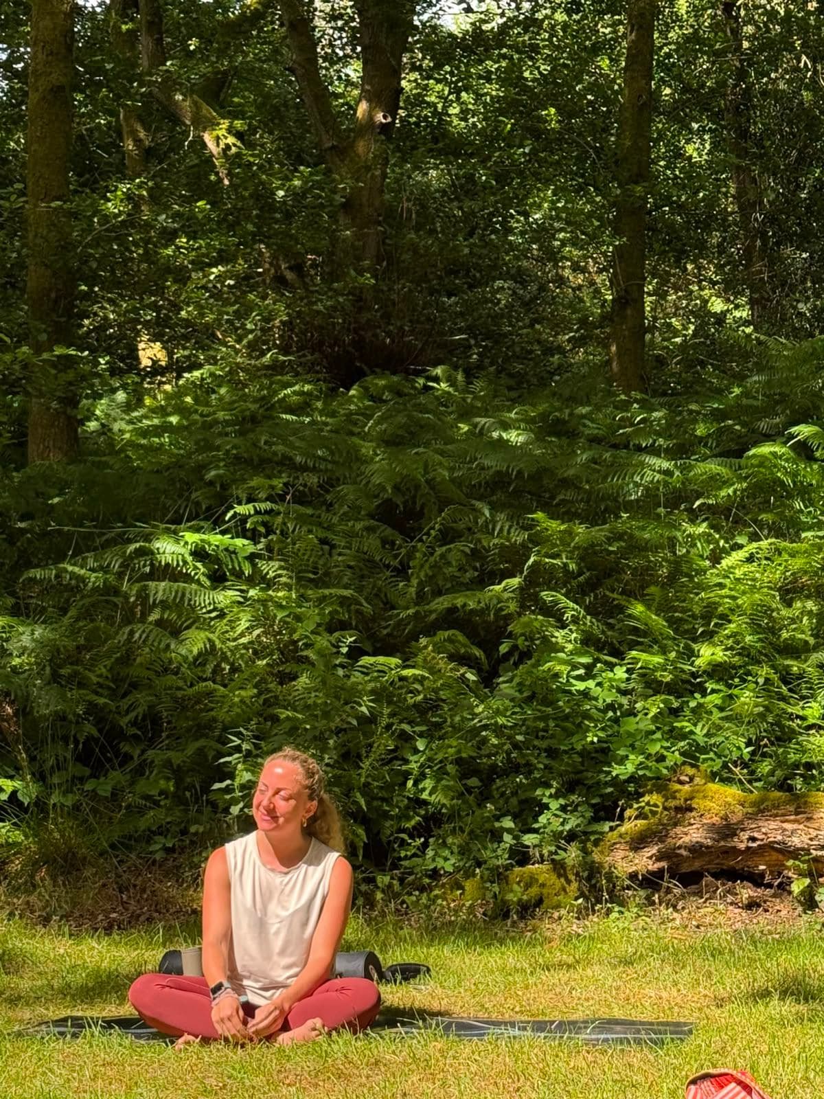 A woman sitting cross-legged and smiling in front of ferns