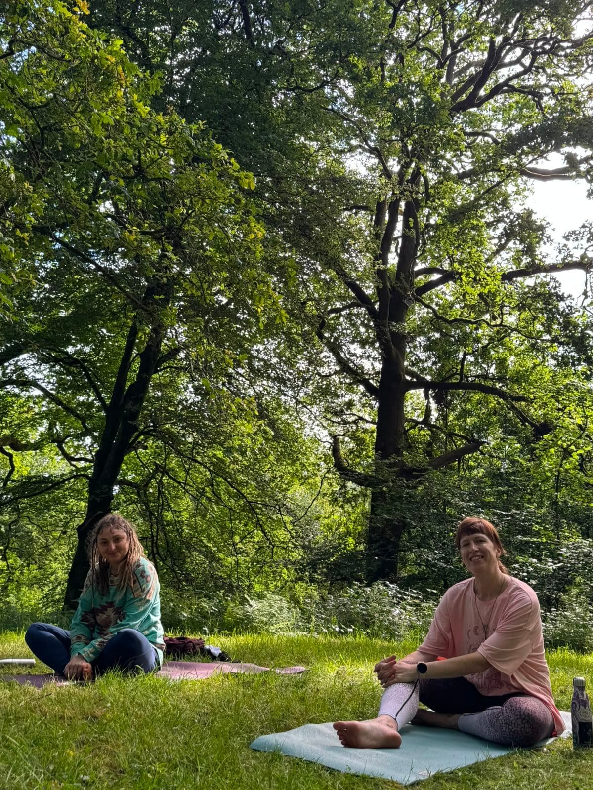 Two women sitting together on mats beneath the trees